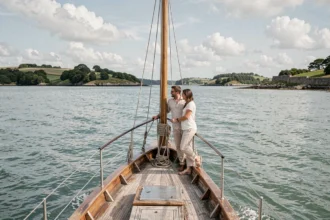 Couple à bord d'un voilier traditionnel naviguant dans le golfe du Morbihan avec des îles verdoyantes en arrière-plan