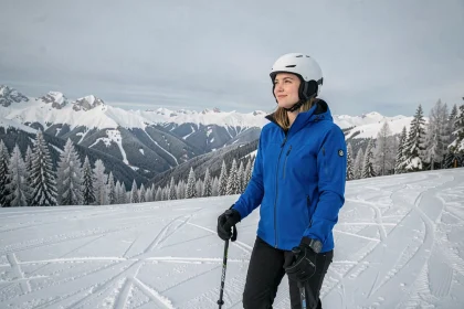 Jeune femme en veste de ski bleue au sommet d'une piste enneigée avec vue panoramique sur les montagnes